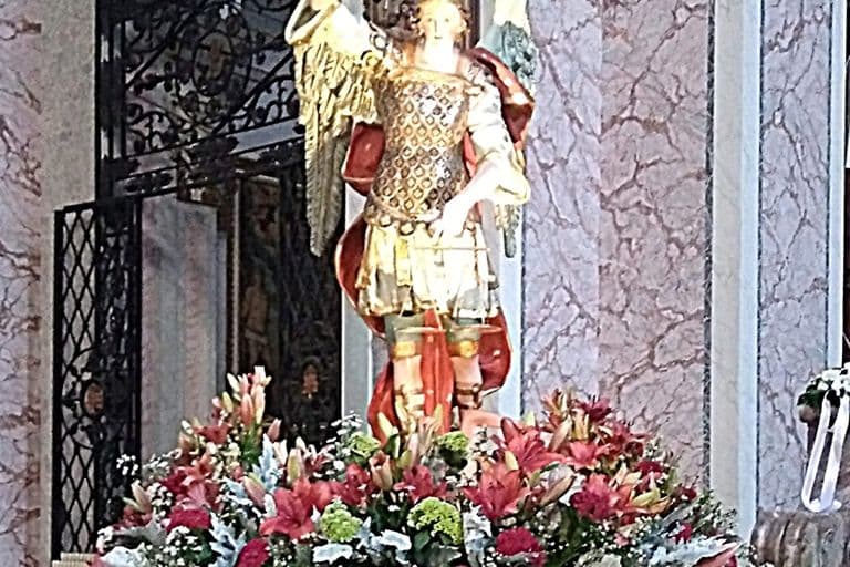 La statua di San Michele Arcangelo con la composizione di fiori e i ceri